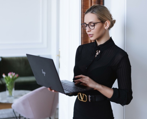 eine frau in einem schwarzen kleid benutzt einen laptop in einem raum mit einem rosa stuhl und einem tisch