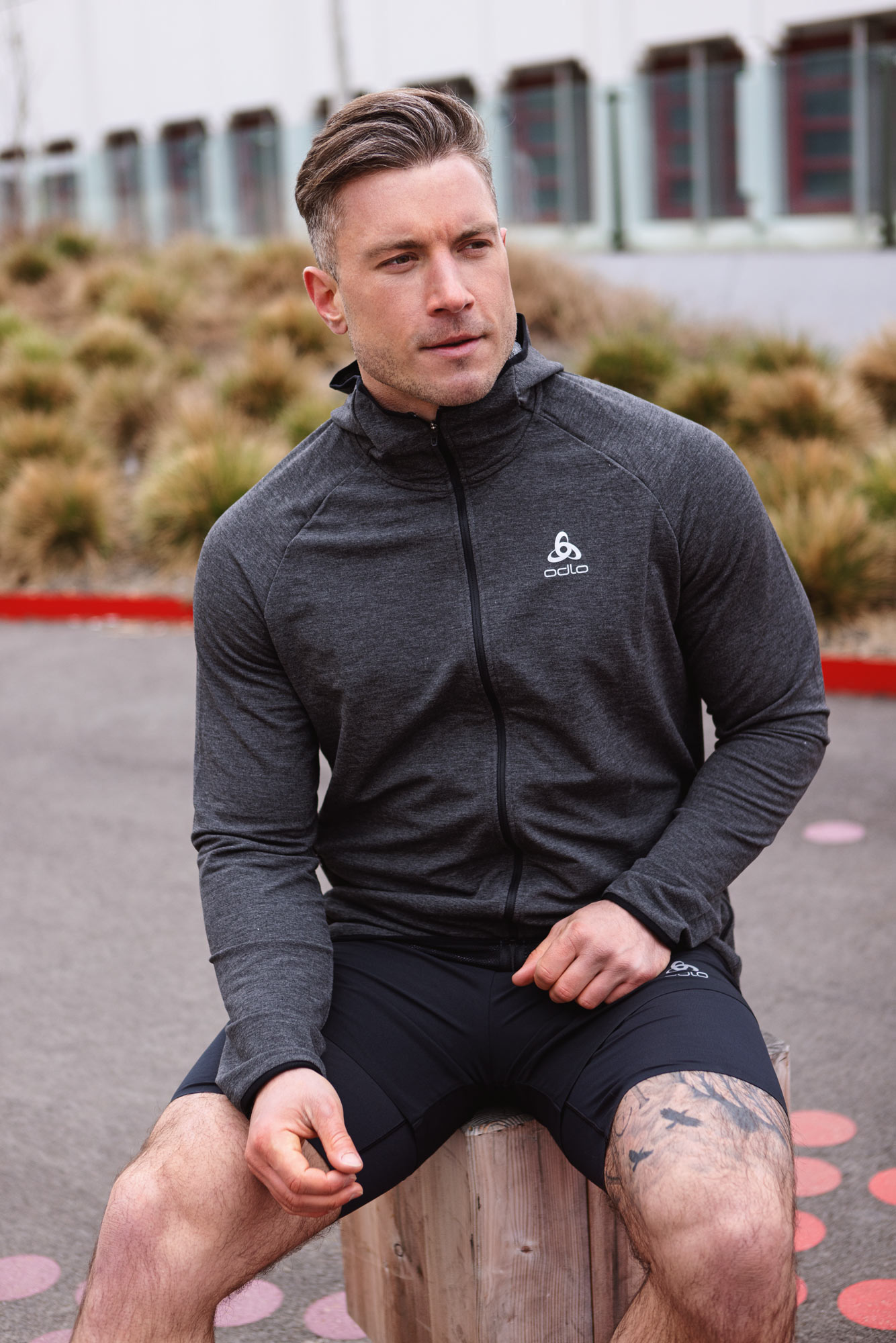 Ein männliches Fitnessmodel sitzt auf einer Bank in grauen Fitness