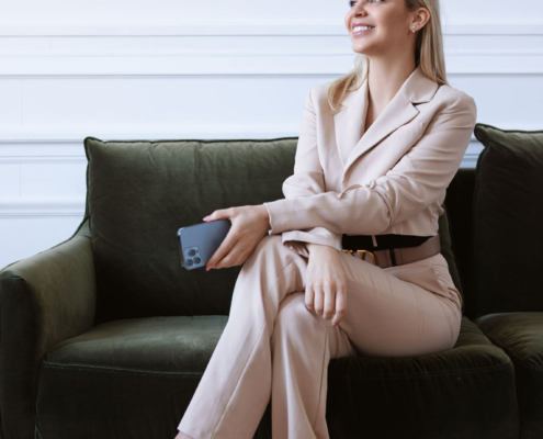 Eine Frau, die mit einem Smartphone in der Hand auf einer Couch sitzt und in die Kamera lächelt