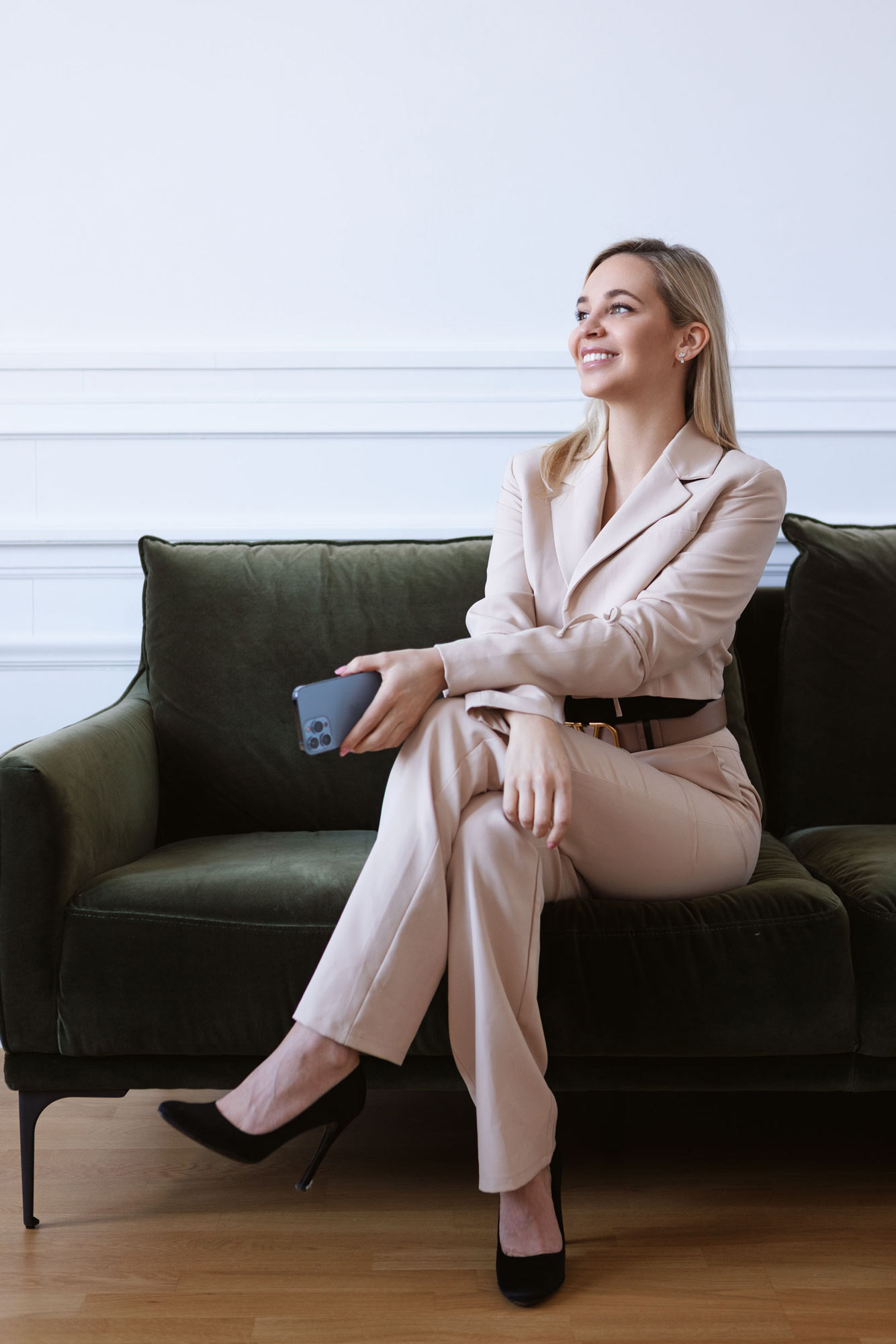 Eine Frau, die mit einem Smartphone in der Hand auf einer Couch sitzt und in die Kamera lächelt