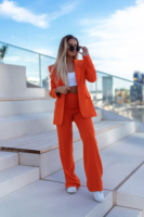 Ein weibliches Fashion Model in einem orangen Anzug und weißen Shirt steht auf Stiegen und blickt in die Ferne