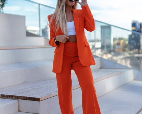 Ein weibliches Fashion Model in einem orangen Anzug und weißen Shirt steht auf Stiegen und blickt in die Ferne
