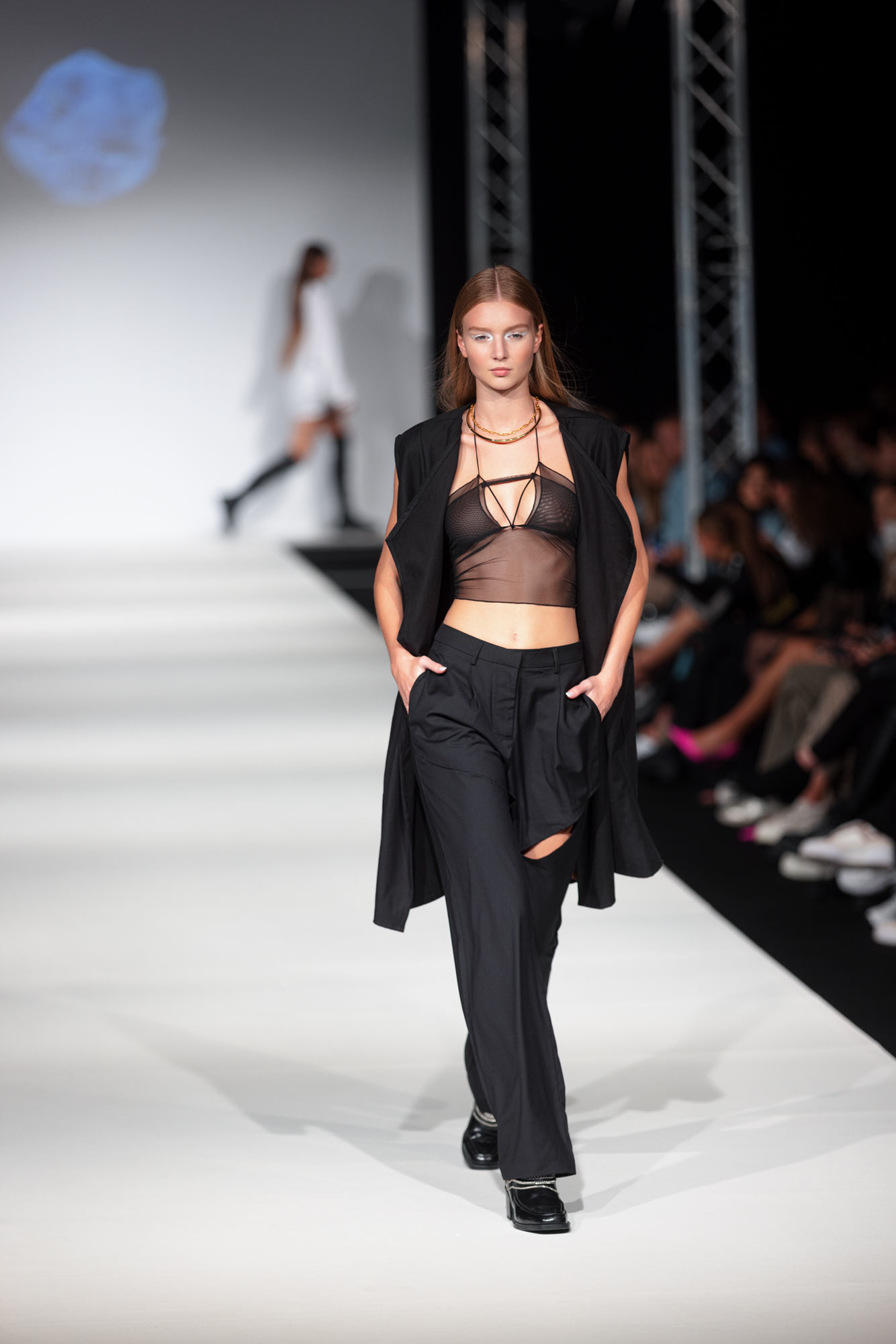 Ein Model in einem schwarzen Outfit und einem schwarzen BH geht einen Laufsteg auf der Vienna Fashion Week entlang
