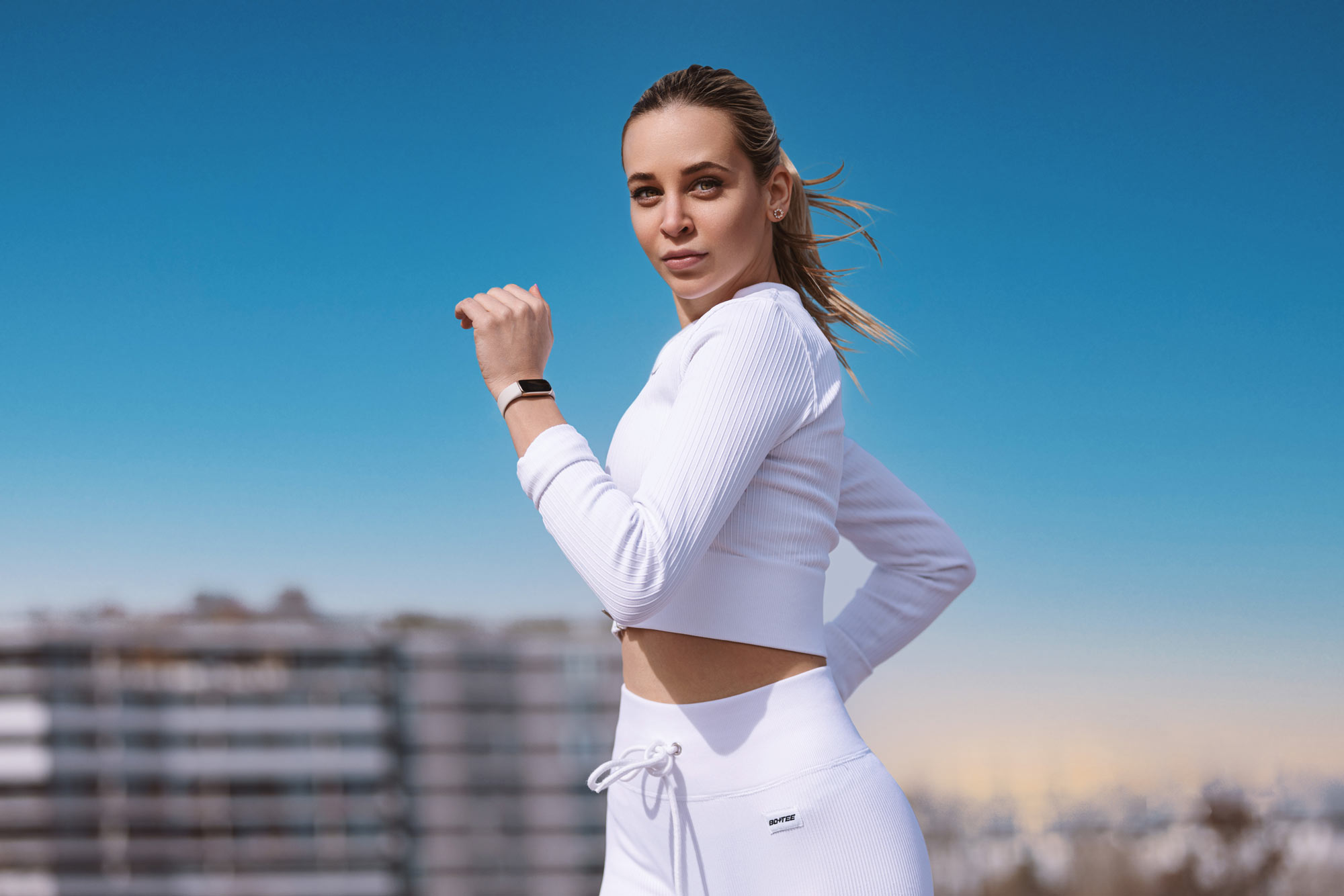 Ein weibliches Fitness Model in weißen Sport Outfit läuft auf der Straße