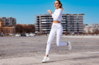 Ein weibliches Fitness Model in weißen Sport Outfit läuft auf der Straße