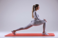 Eine Frau in einem weißen Oberteil und einer grauen Hose macht mit gebeugten Beinen eine Yoga-Pose auf einer roten Matte